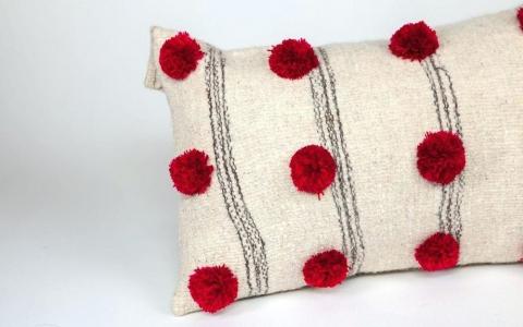 white pillow with black stripes and red pompoms 