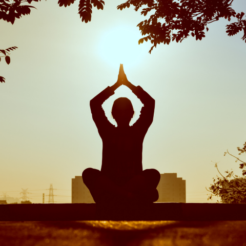 Silhouette of person sitting and meditating outside 