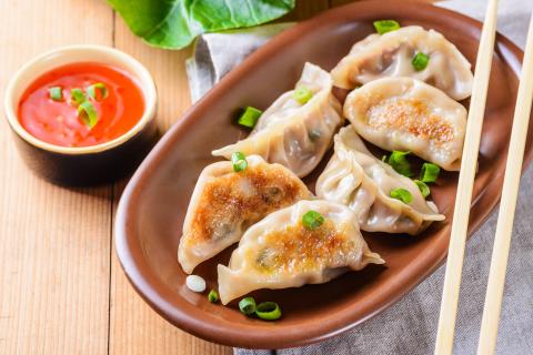 a plate of dumplings with chopsticks and dipping sauce on table