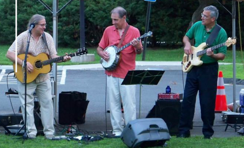 Three musicians outdoors with guitars and banjo