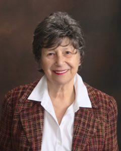 A professional headshot of a woman with short brown hair, she is wearing a plaid jacket and a white collared shirt. 