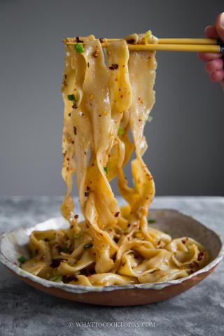 hand pulled noodles that have a spices or a spice sauce on them. They are being lifted out of the bowl/dish by a pair of wooden chopsticks and showing off the texture of the noodles