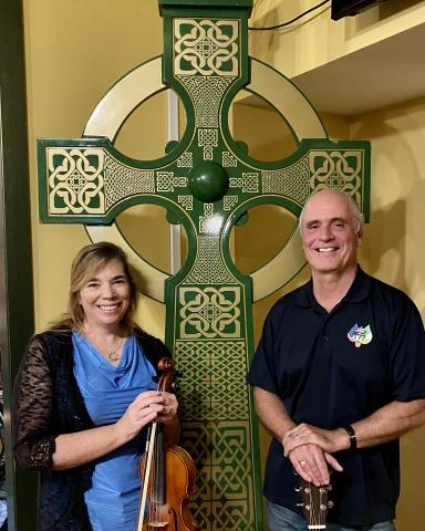 two people standing with a tall Celtic cross sculpture between them