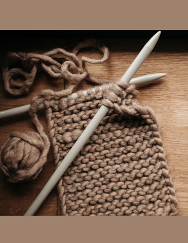 knitting needles making a brown yarn project against a wood background and top & bottom boarders that is a dark chocolately brown 