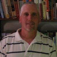 a man with a white and black stripped shirt sitting in a chair, headshot