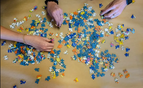 three hands over a pile of jigsaw pieces