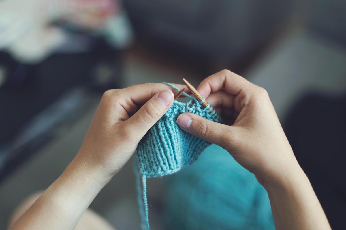 Two hands knitting a blue piece together