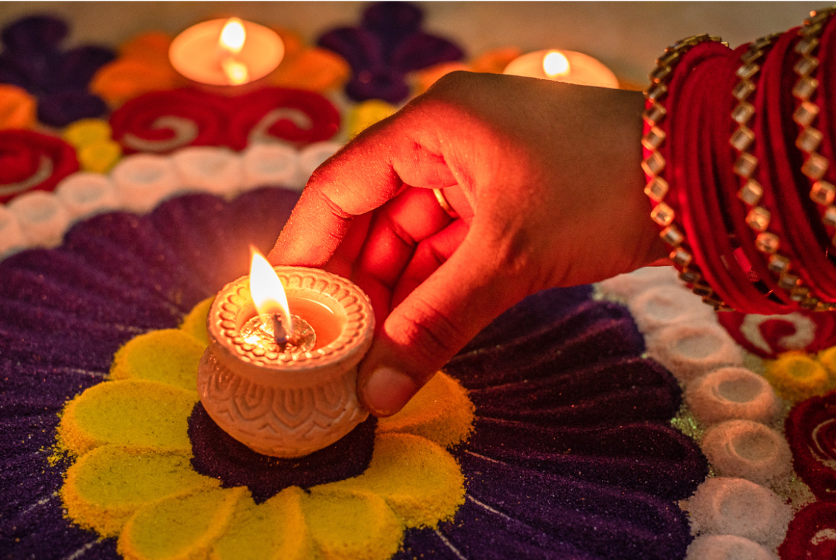 Lit Diya (clay lamp) inside a rangoli (sand art) with hand 