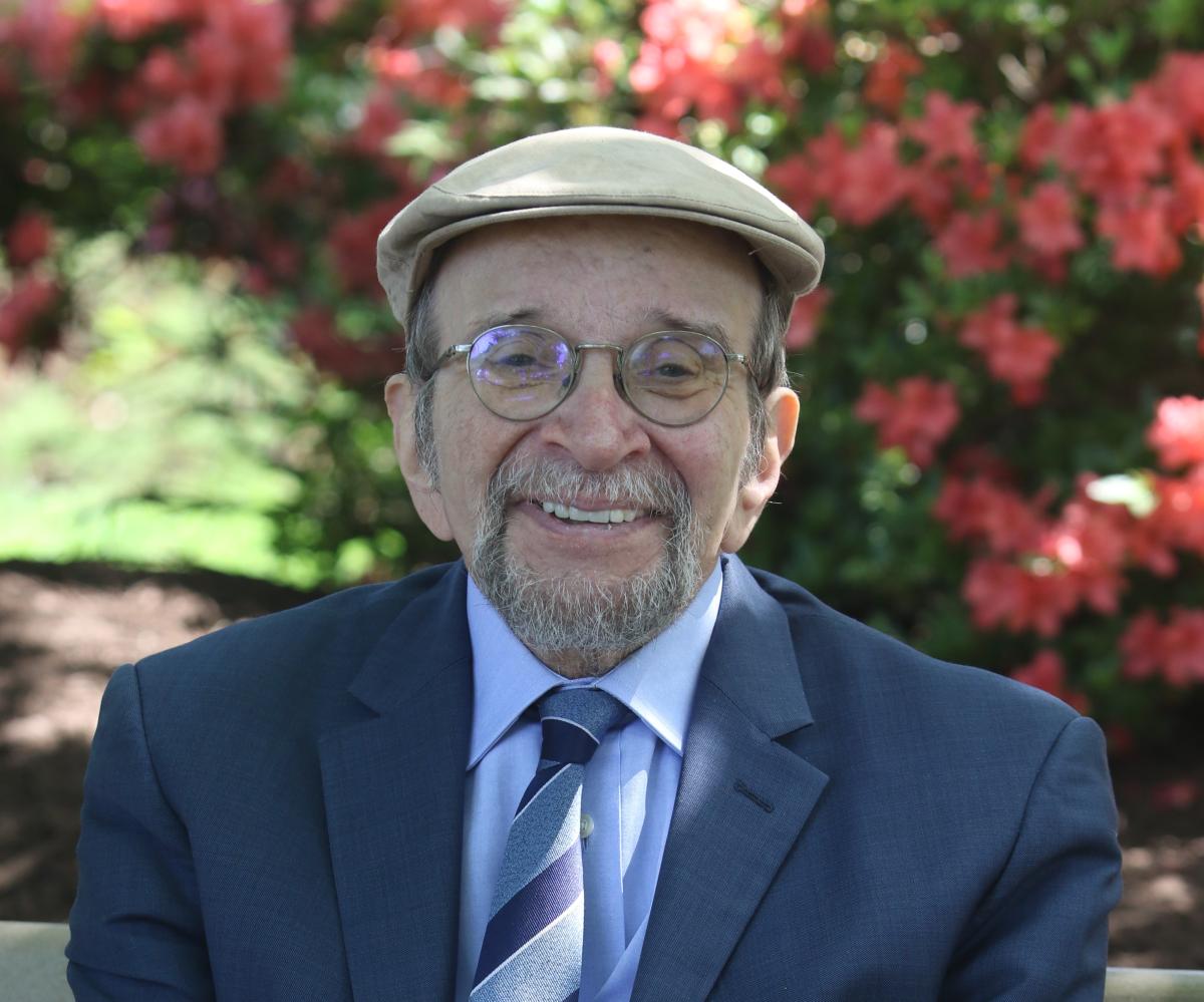 an older man against a flower background with a cap and glasses